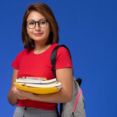 vista-frontal-estudiante-camisa-roja-mochila-sosteniendo-libros-archivos-sonriendo-pared-azul
