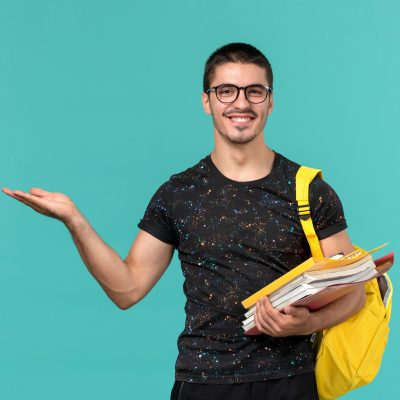 vista-frontal-estudiante-camiseta-oscura-mochila-amarilla-sosteniendo-archivos-libros-sonriendo-pared-azul-claro