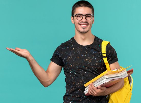vista-frontal-estudiante-camiseta-oscura-mochila-amarilla-sosteniendo-archivos-libros-sonriendo-pared-azul-claro